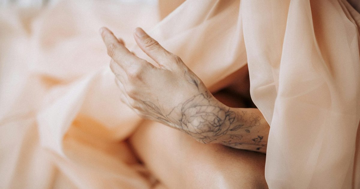 pexels-photo-10141587-10141587 Close-up of a tattooed hand gracefully posed with sheer fabric, evoking elegance and artistry.