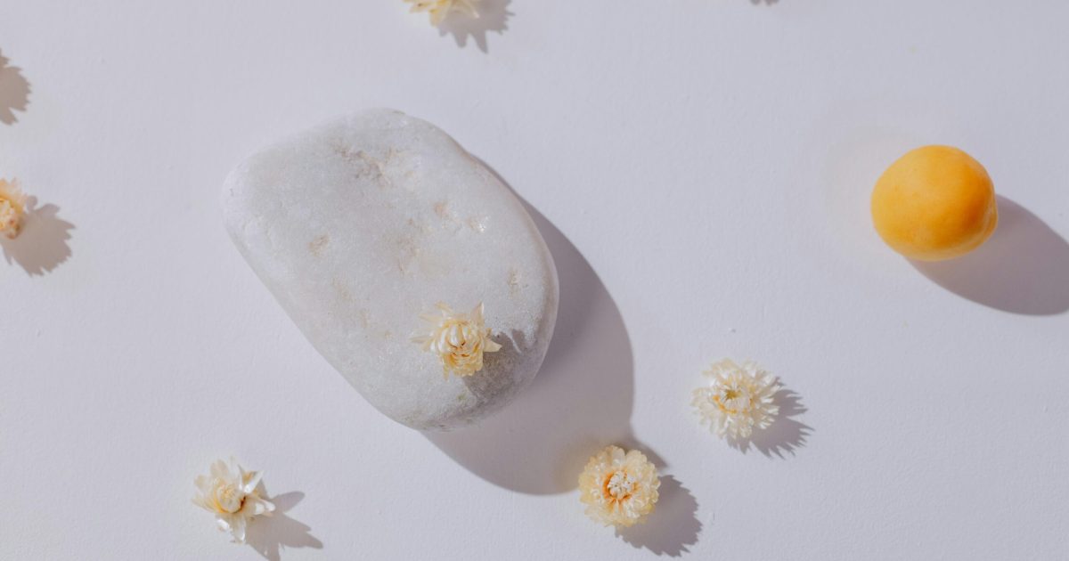 A serene minimalist arrangement featuring a stone and delicate flowers on a white background.