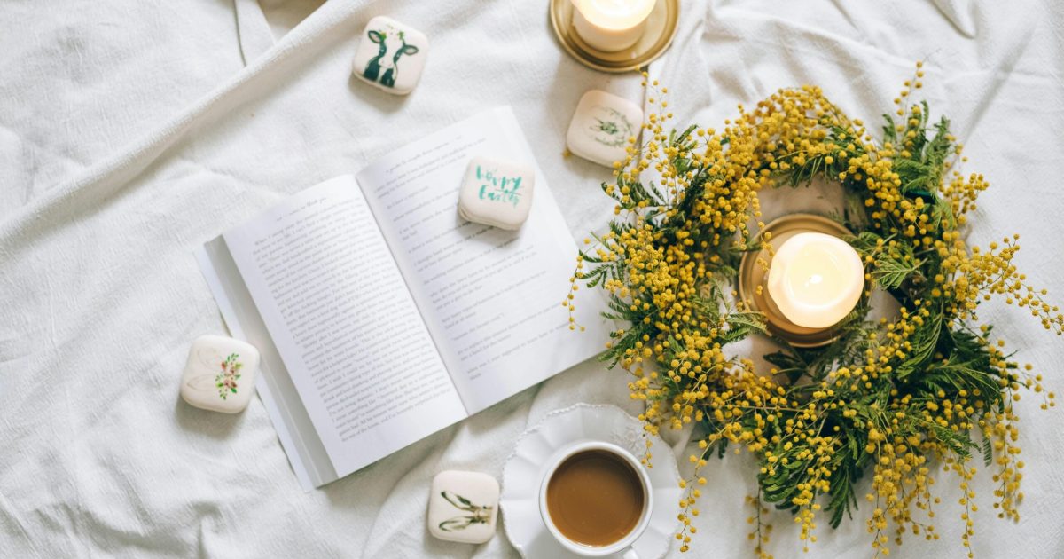 pexels-photo-6560996-6560996 A cozy flatlay featuring an open book, candle, and coffee on white bedding with yellow flowers.